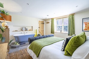 A bedroom with a large bed, a bathtub, and a window with curtains.
