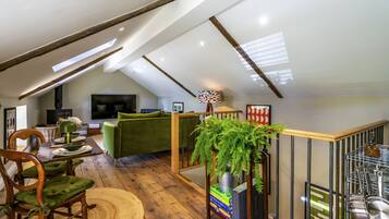 A loft-style living space with a dining area, green sofa, and a staircase.