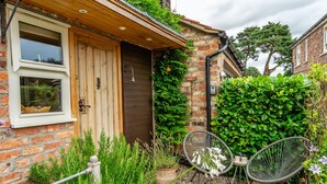 A rustic brick house with a wooden door, a small garden with potted plants, and two metal chairs. - Haxby Hayloft: A Charming Countryside Retreat Near York (York)