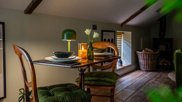 A dining area with a wooden table, chairs, a candle, and a green lamp. - Haxby Hayloft: A Charming Countryside Retreat Near York (York)