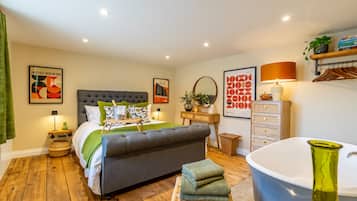 A bedroom with a large bed, a bedside table, a lamp, a mirror, a dresser, and a bathtub.