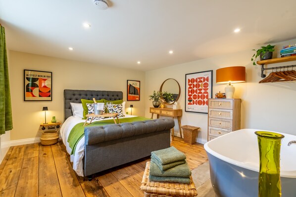 Une chambre à coucher avec un grand lit, une table de chevet, une lampe, un miroir, une commode et une baignoire.