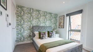 A bedroom with a large bed, floral wallpaper, and a window with a view of a brick building. - Bootham Row 8: A Cozy City-Centre Retreat in York (York)