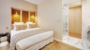 Un dormitorio moderno con una cama grande, lámparas de noche, una mesita de noche y un baño de mármol con ducha.