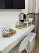 Un escritorio blanco con una cafetera, un hervidor, una bandeja con aperitivos y un juego de vasos.