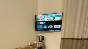 A small, modern room with a wooden desk, a white chair, a television mounted on the wall, a coffee maker, and a mini-fridge. - Center Rooms La Spezia  (La Spezia)