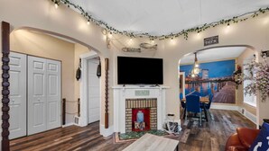 Een woonkamer met een open haard, een televisie en een eetgedeelte met blauwe stoelen.