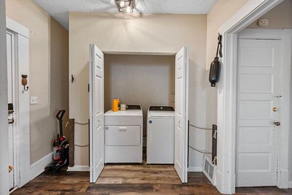 A laundry room with two stacked washer and dryer units, a vacuum cleaner, and a heater on the floor.