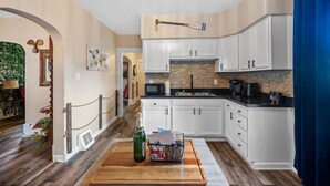 Een moderne keuken met witte kastjes, een zwart aanrecht en een houten snijplank met een fles en papieren.