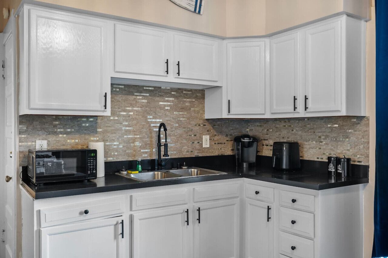 A kitchen with white cabinets, a black countertop, a microwave, a coffee maker, and a sink.
