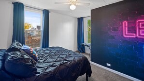 Une chambre à coucher avec un lit, un ventilateur de plafond, un néon mural et une vue sur l’extérieur.