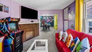 Une pièce avec un canapé rouge, un téléviseur fixé au mur et des jeux d’arcade.