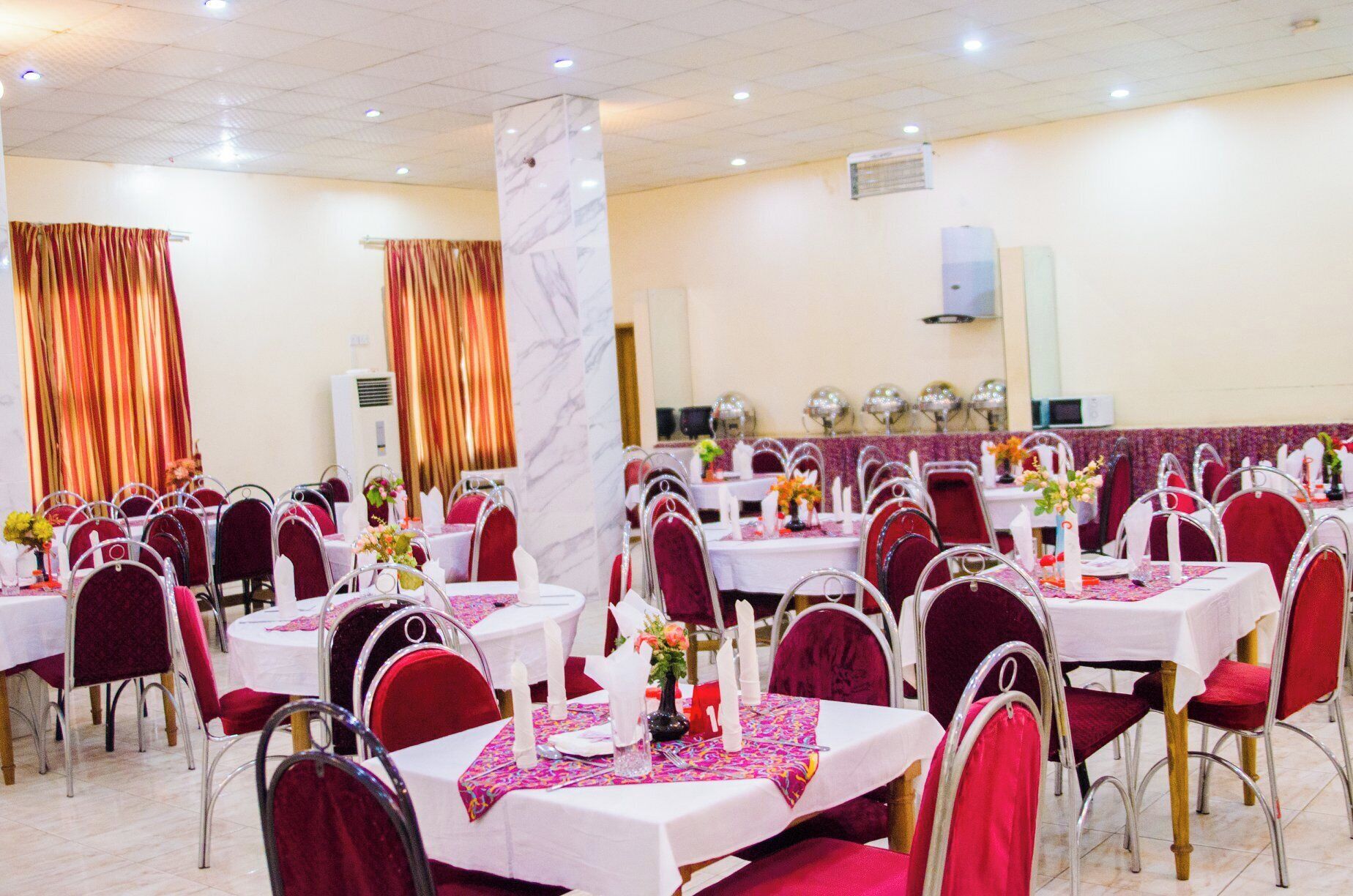 Un salón de banquetes con mesas redondas, sillas rojas y manteles blancos.