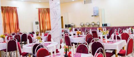 Un salón de banquetes con mesas redondas, sillas rojas y manteles blancos.