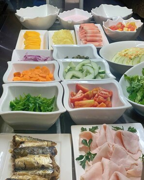 Un buffet proposant une variété d’aliments, notamment des fruits, des légumes et des viandes coupés en tranches.