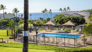 A pool area with lounge chairs and umbrellas, surrounded by palm trees and a view of the ocean. - Hale Kamaole #124 Ground floor condo, easy access to best beach on Maui! (Kihei)