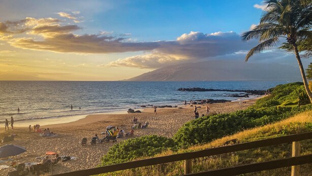 A beach with people, umbrellas, and a wooden fence. - Hale Kamaole #124 Ground floor condo, easy access to best beach on Maui! (Kihei)