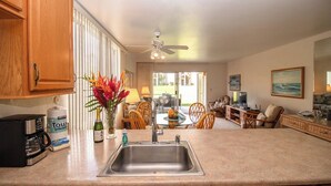 A kitchen with a stainless steel sink, wooden cabinets, a coffee maker, and a vase with flowers. - Hale Kamaole #124 Ground floor condo, easy access to best beach on Maui! (Kihei)