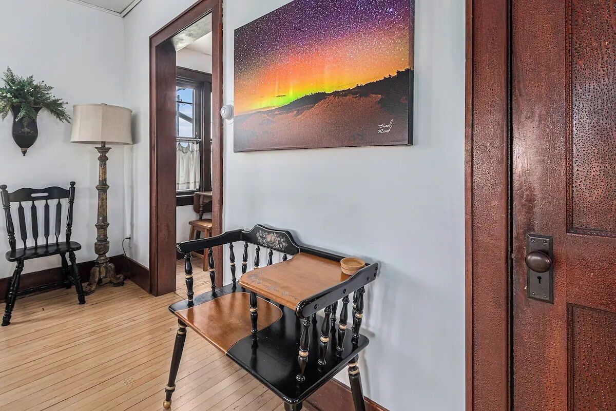A room with a wooden floor, a black and wooden chair, a lamp, and a painting of a night sky.