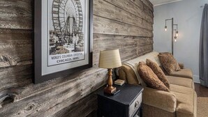 Quarto com parede de madeira, quadro emoldurado de uma roda gigante, luminária e sofá com almofadas estampadas.