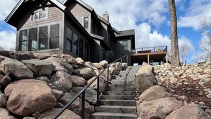 Una escalera conduce a una casa con barandilla de piedra, rodeada de rocas grandes y un cielo despejado.