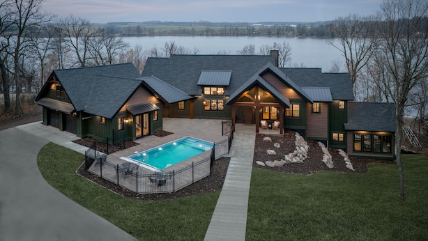 Una casa grande con piscina, un porche cubierto y vista a un lago.