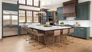 Una cocina moderna con una isla central, taburetes de bar, electrodomésticos de acero inoxidable y armarios oscuros.