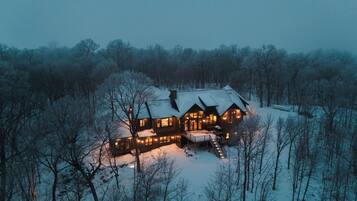 A large log cabin with multiple windows and a covered porch, surrounded by a snowy forest.