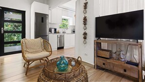 Een moderne woonkamer met een rieten stoel, een tv-meubel met decoratieve objecten, en een keuken op de achtergrond.