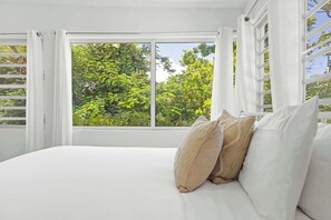 A bedroom with a large window, white curtains, and a bed with white and beige pillows. - La Casita de Rio Grande | Nature Lovers' Paradise (Río Grande)