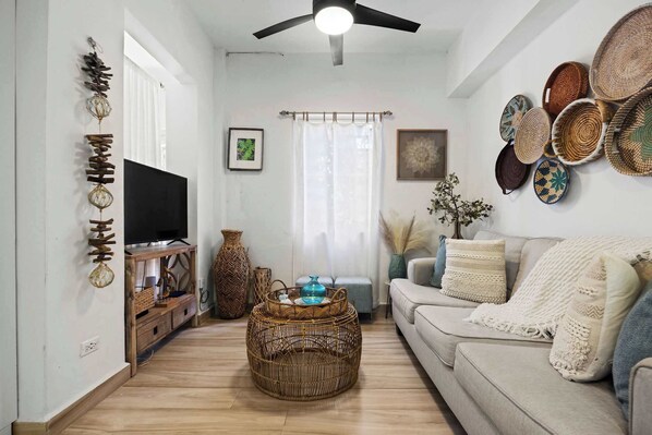 A living room with a sofa, a television, a coffee table, and decorative baskets on the wall. - La Casita de Rio Grande | Nature Lovers' Paradise (Río Grande)