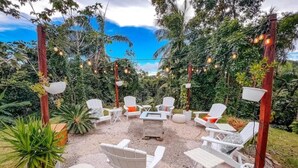 Een terras met witte stoelen en tafels, omringd door groen en decoratieve verlichting.