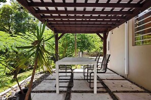 A covered patio area with a table and chairs, surrounded by greenery and a stone pathway. - La Casita de Rio Grande | Nature Lovers' Paradise (Río Grande)