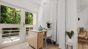Een kamer met een houten bureau, een witte stoel, een klein wit tafeltje met een vaas en een rieten stoel.