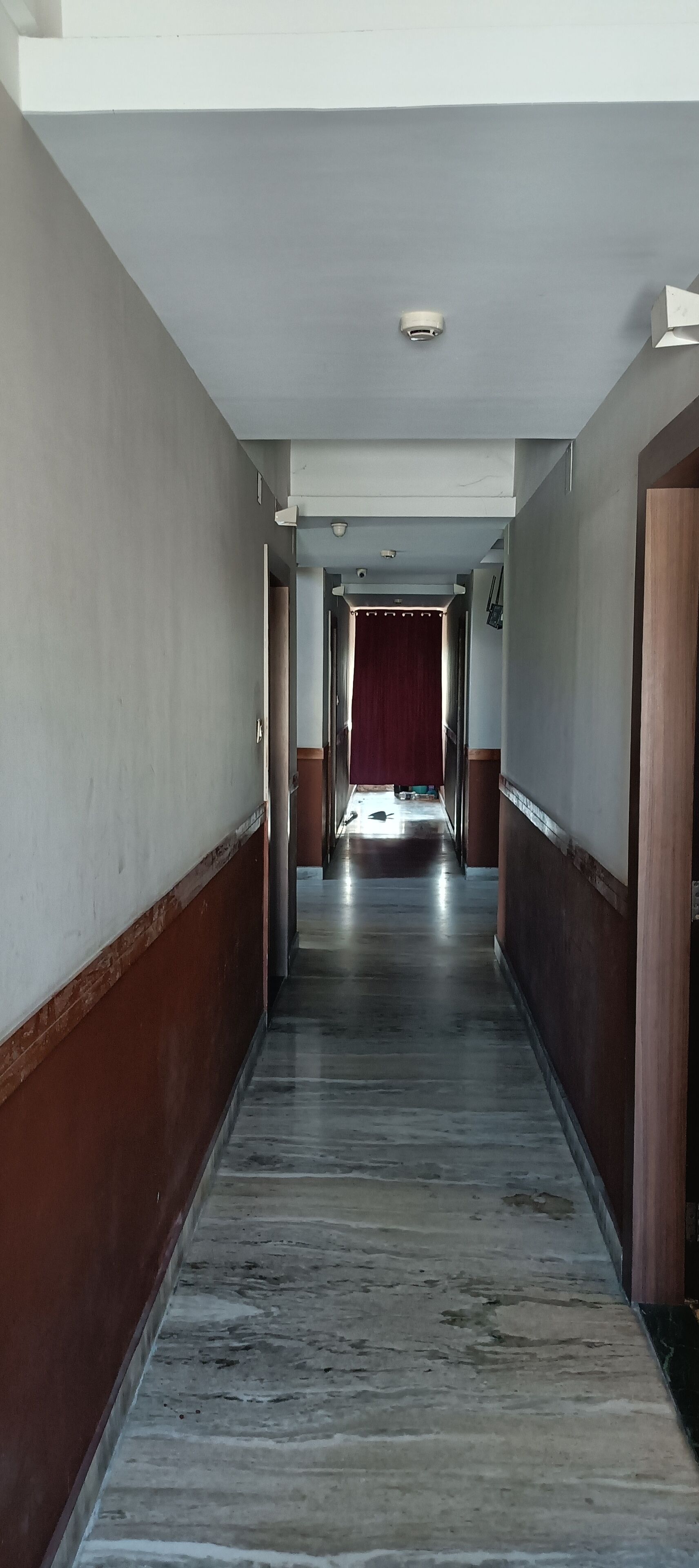 Um corredor longo e estreito com piso de mármore e lambris de madeira nas paredes.