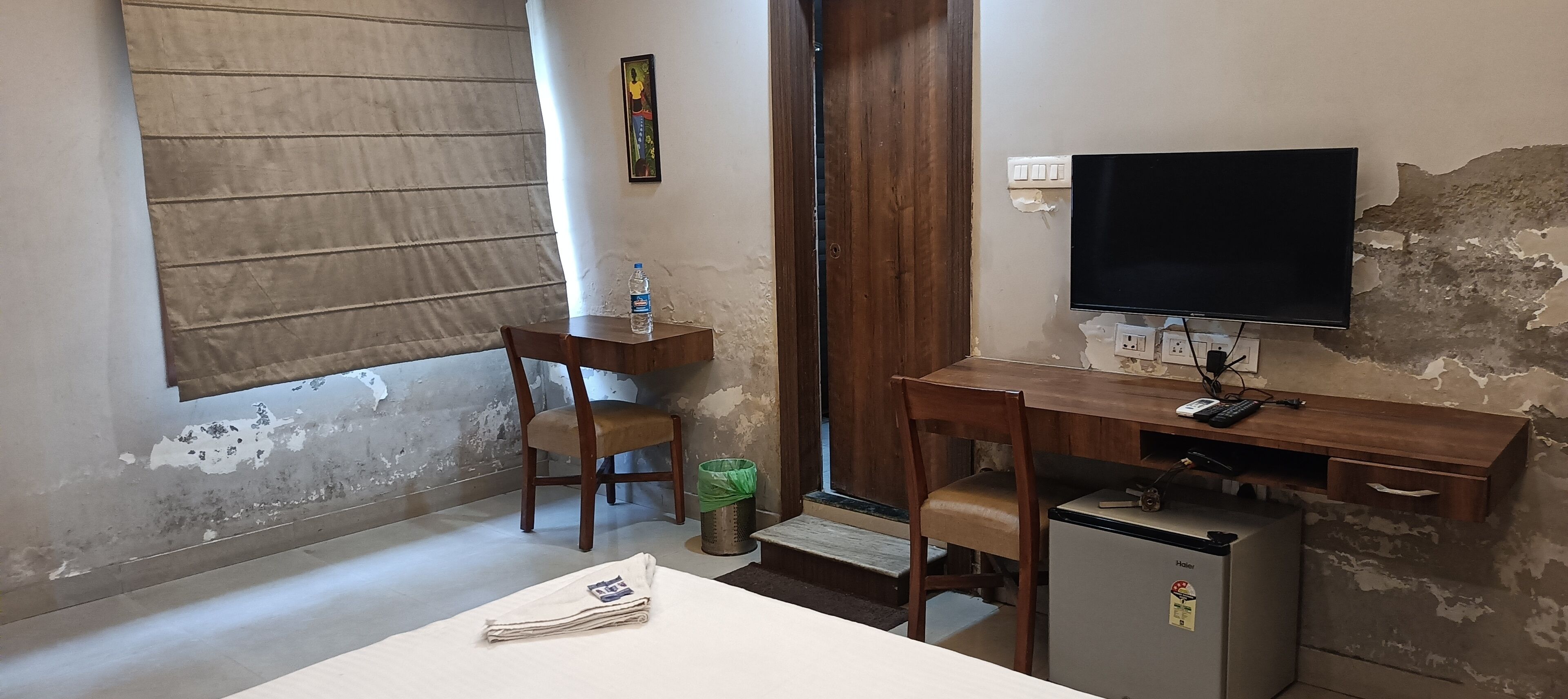 Une petite pièce, de taille modeste, comprenant un bureau, une chaise, un téléviseur et un réfrigérateur.