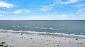 A beach with a wide sandy area, a few small structures, and the ocean in the background.