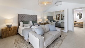 A modern bedroom with a large bed, a sofa, and a bathroom visible through a glass door. - Villa Bellagio - Rent Villas Lanzarote (Playa Blanca)