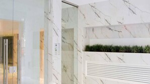 Ένας μοντέρνος εσωτερικός χώρος με μαρμάρινοι τοίχοι, μια είσοδος με γυάλινη πόρτα και μια εντοιχισμένη ζαρντινιέρα με φυτά.
