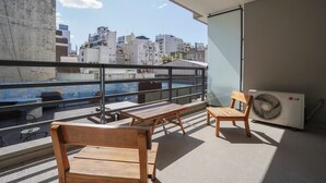 Ένα μπαλκόνι με έπιπλα από ξύλο, μια μονάδα κλιματισμού και θέα στην πόλη.