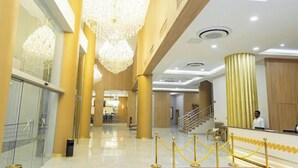 A hotel lobby with chandeliers, a reception desk, and a staircase.
