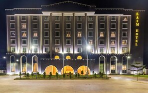 Un hôtel à plusieurs étages, doté d’une façade symétrique, de grandes fenêtres et d’une entrée imposante avec des fenêtres en arc de cercle.