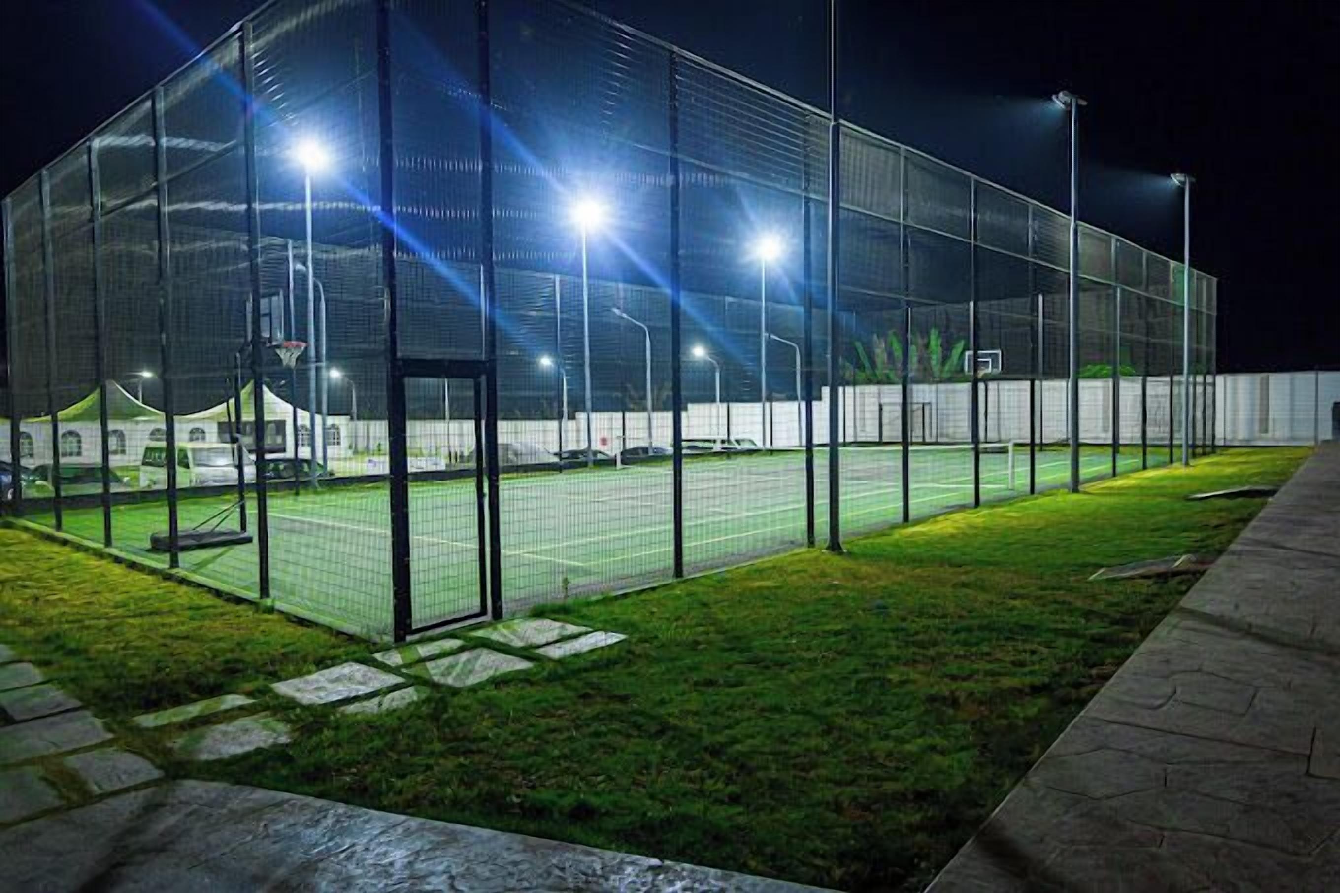 Een sportfaciliteit met een omheind tennisveld, een overdekte tribune en een goed verlichte omgeving.