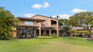 Ein zweistöckiges Haus mit überdachter Veranda, Rasen und tropischen Pflanzen.