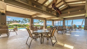 Ein großzügiger Außenbereich mit Tischen und Stühlen, mit Blick auf einen Pool und das Meer.