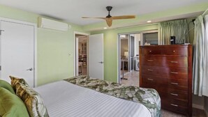 A bedroom with a bed, a wooden dresser, a ceiling fan, and a closet. - Beachfront Escape at Royal Mauian #207 – Unmatched Ocean Views and Comfort! (Kihei, Maui)