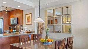 A modern kitchen with wooden cabinets, a stainless steel refrigerator, and a fruit bowl on the island. - Beachfront Escape at Royal Mauian #207 – Unmatched Ocean Views and Comfort! (Kihei, Maui)