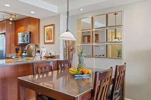 A modern kitchen with wooden cabinets, a stainless steel refrigerator, and a fruit bowl on the island. - Beachfront Escape at Royal Mauian #207 – Unmatched Ocean Views and Comfort! (Kihei, Maui)