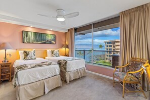 Ein Hotelzimmer mit zwei Betten, einem großen Fenster mit Balkon, einem Deckenventilator und Blick auf ein Gebäude gegenüber dem Wasser.