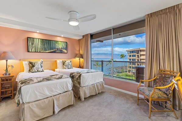 A hotel room with two beds, a large window with a balcony, a ceiling fan, and a view of a building across the water. - Ultimate Oceanfront Paradise-Spectacular Ocean Views-Mana Kai Maui Resort 405C (Kihei, Maui)